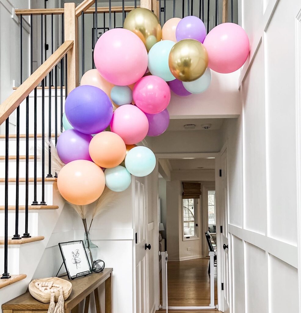 Pink, purple, blue and orange balloon garland hanging from stairs.