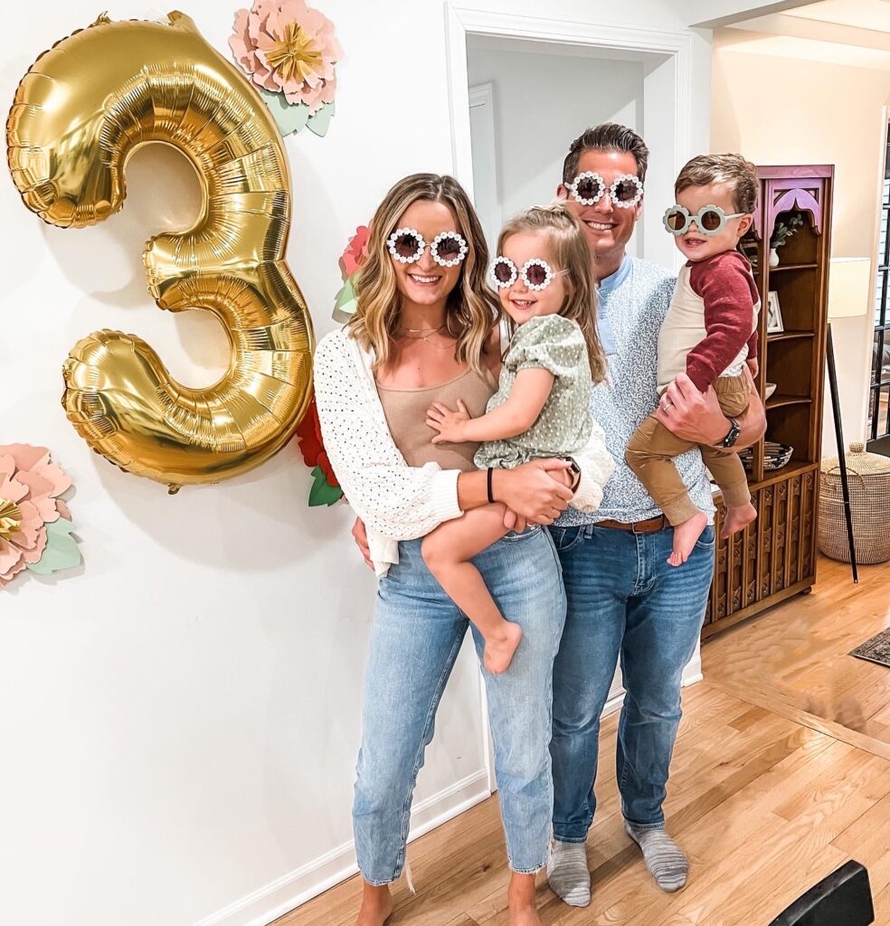 Our whole family wearing flower sunglasses in front of a 3 balloon.